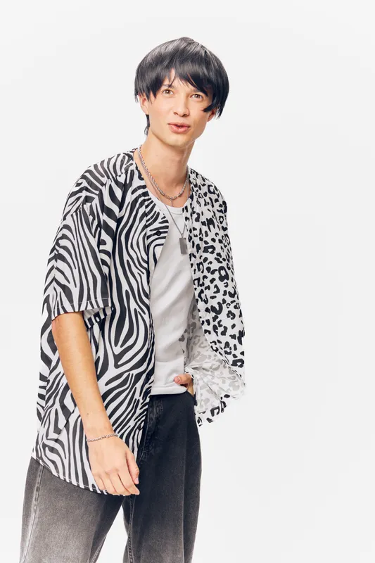 Young man wearing a stylish black and white patterned shirt with zebra and leopard prints, posing confidently on a clean white background.