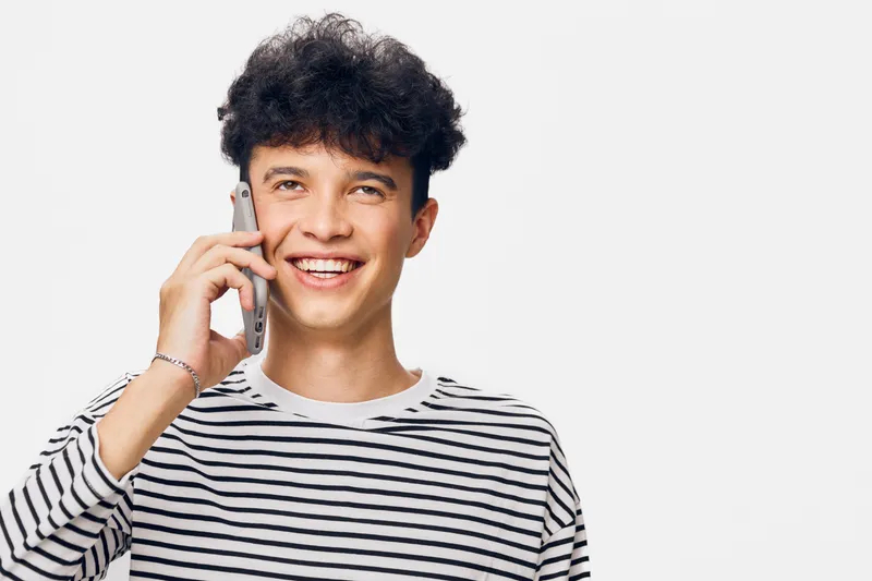 smiling man talking on phone wearing striped shirt, young happy male with curly hair on white background in casual style