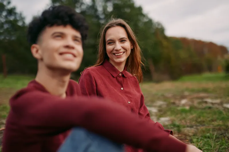 Two relaxed individuals share a quiet moment outdoors, conveying authenticity through natural interaction, genuine emotion, and candid connection in a sunlit park during autumn warmth.