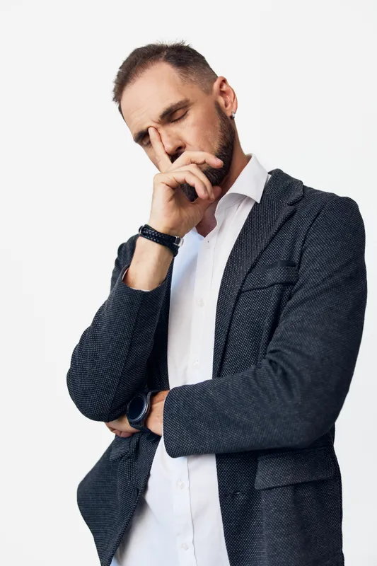 A focused business man stands against a colored plain background, expressing thoughtful emotion. He embodies professionalism, determination, and calm confidence.