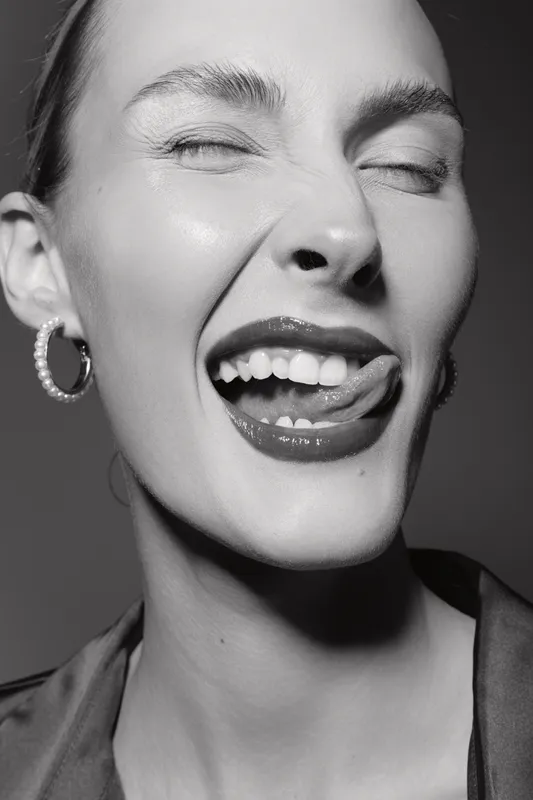 Young white woman with fair skin making a playful face with tongue out and eyes closed in black and white portrait.