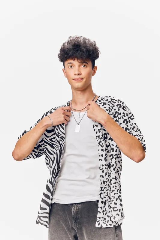 young man wearing animal print shirt and white t-shirt posing confidently against plain white background with casual hairstyle and silver accessories