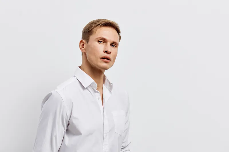 Elegant man with light brown hair wearing a white shirt looking serious pose isolated on a plain white background studio portrait. People style concept