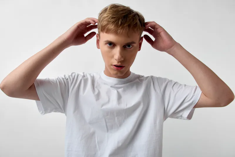 Man adjusting his hair in a white tshirt, studio setup, casual fashion and grooming, confident expression, clean background, suitable for lifestyle, beauty or fashion stock use