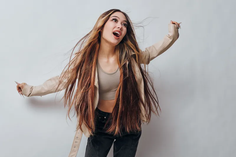 Young woman with long dreadlocks and casual outfit posing and dancing in studio for fashion, peace, lifestyle and freedom with joyful expression on gray background.