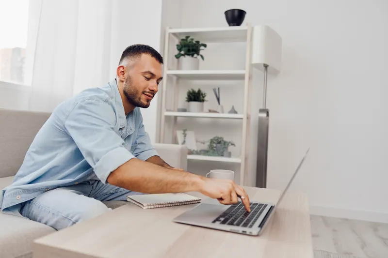Engaged man working on a laptop at home, wearing casual attire. The bright and modern interior creates an inspiring work environment for productivity and creativity.