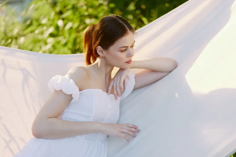 Young woman in white dress, gentle emotions, relaxing outdoors in a serene setting, soft colors, capturing tranquility and nature