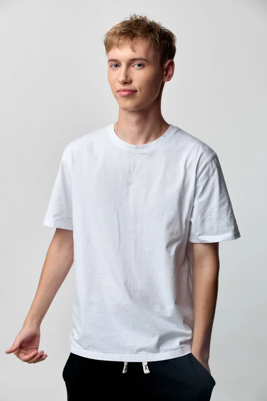 Young man in white tee stands in a light studio, relaxed pose, casual fashion, minimal background, everyday style, clean lines and natural expression in a simple approachable image