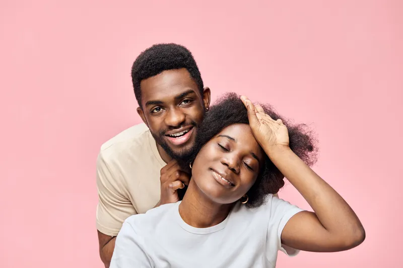 Happy African couple enjoying each other s company, dressed casually, with a joyful expression on a soft pink background, perfect for love and relationship themes