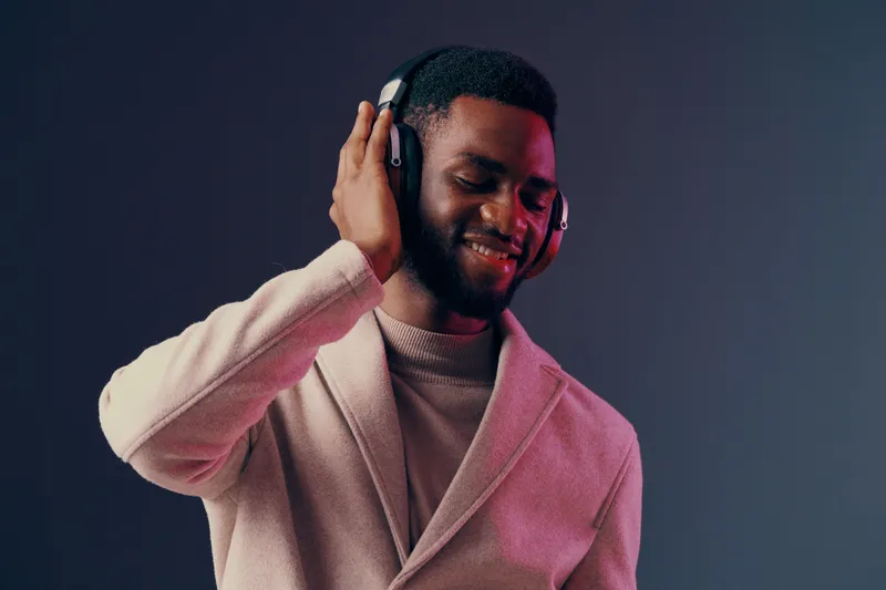 Young African man enjoying music with headphones in a stylish outfit, showcasing happiness and a modern vibe against a colorful gradient background