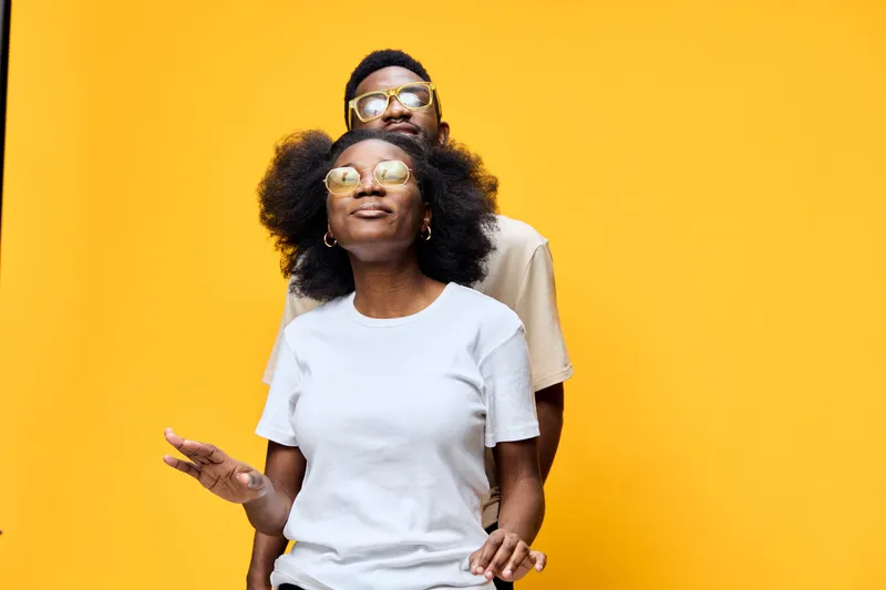 Cheerful young couple enjoying time together against a bright yellow background, showcasing stylish sunglasses and casual outfits, perfect for lifestyle branding