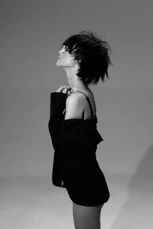 Black and white profile of a young woman wearing sunglasses and an off-shoulder top against a plain background.