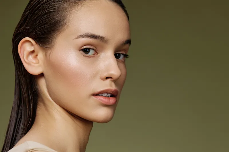 Portrait of a young woman with natural makeup and wet hair against a soft green background, conveying calmness and beauty, perfect for wellness and beauty themes