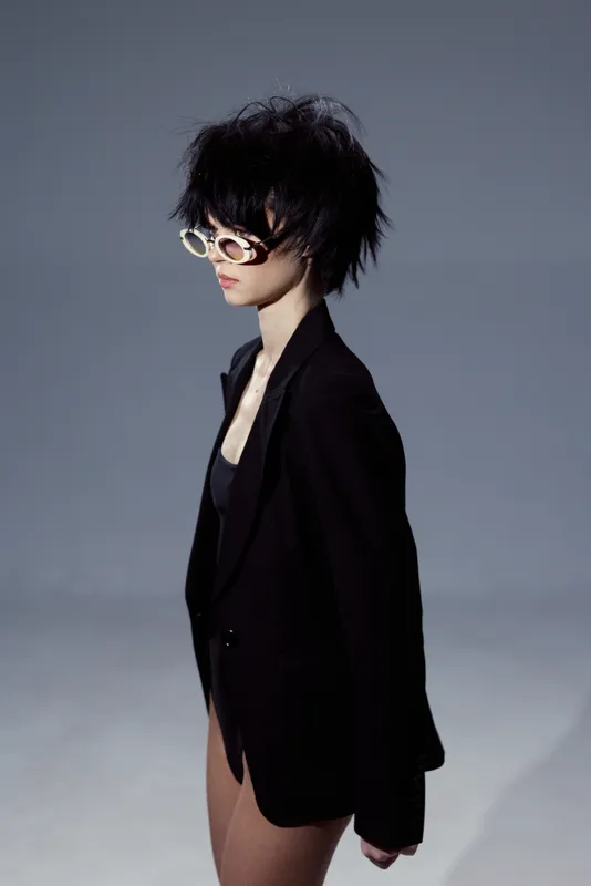 Stylish woman wearing black blazer and sunglasses with short messy hair in minimalistic setting