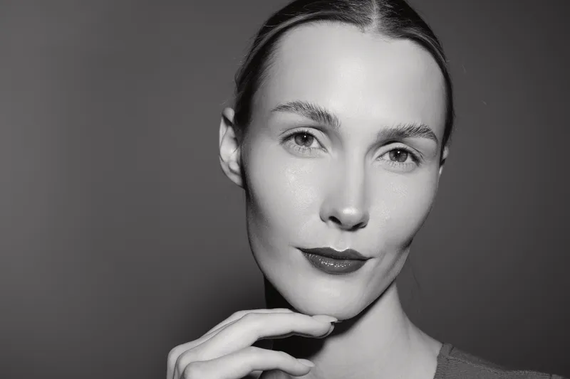 Close up portrait of white woman with pale skin and slicked hair touching chin in studio, calm expression.