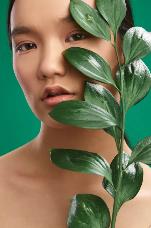 asian woman portrait with lush plant leaves, serene expression, soft studio lighting, botanical theme, vibrant green tones, calm atmosphere, contemporary aesthetic.