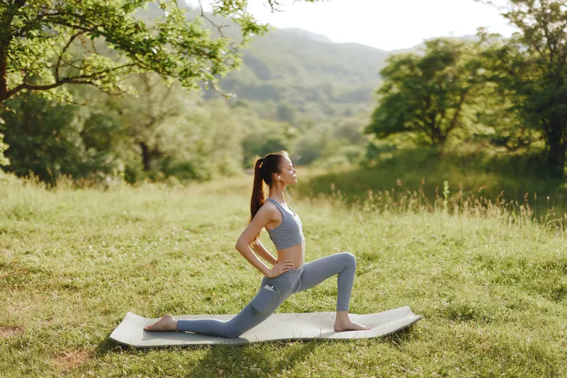 Young woman practicing yoga in a serene outdoor setting, wearing activewear and expressing calmness, surrounded by nature and greenery, showcasing fitness and tranquility