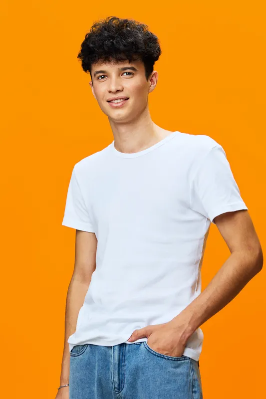 young man wearing white t-shirt standing confidently with hand in pocket against bright orange background, casual style, smiling expression