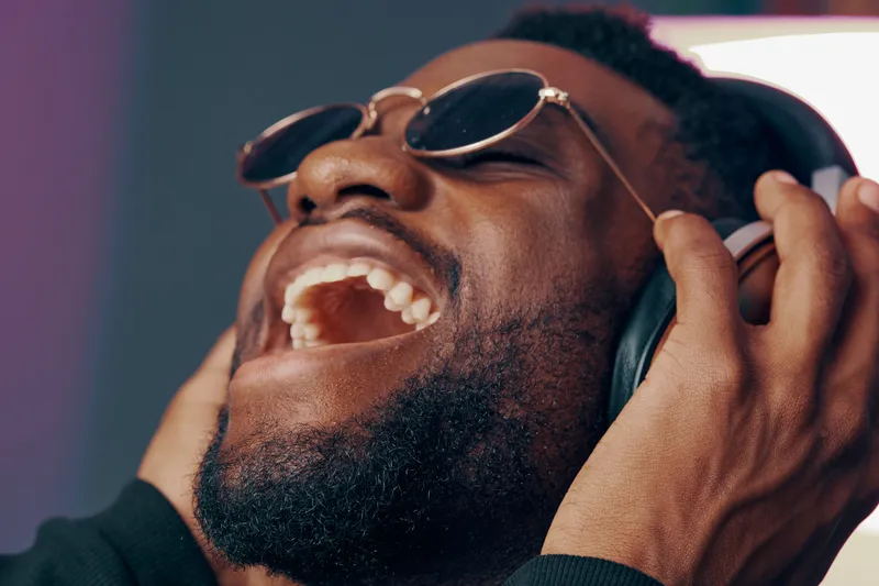 Happy young Black man enjoying music with headphones, expressing joy and excitement, indoors with vibrant background colors, perfect for lifestyle themes