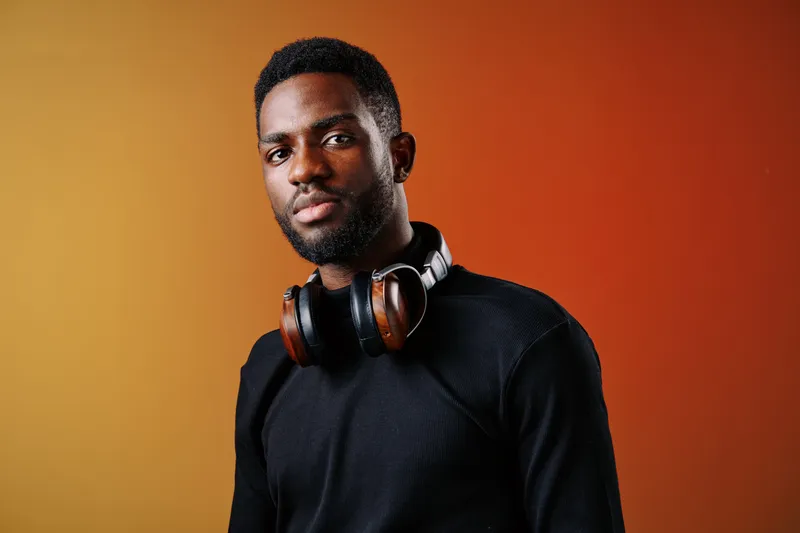A stylish Black man wearing headphones against a vibrant orange background, conveying confidence and passion for music
