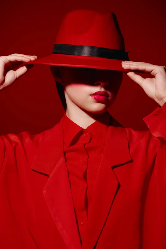 Woman dressed in bright red fashionable clothes and a matching hat partially hiding her face with a mysterious chic style. Intense lighting enhances the elegance and vibrant mood.