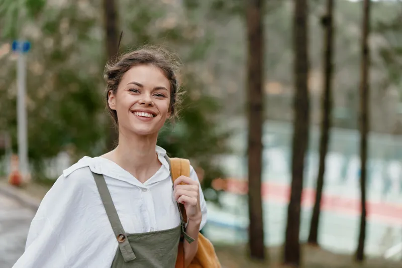 Happy young woman smiling outdoors in casual outfit, enjoying nature in a forest setting during spring, representing joy and carefree lifestyle