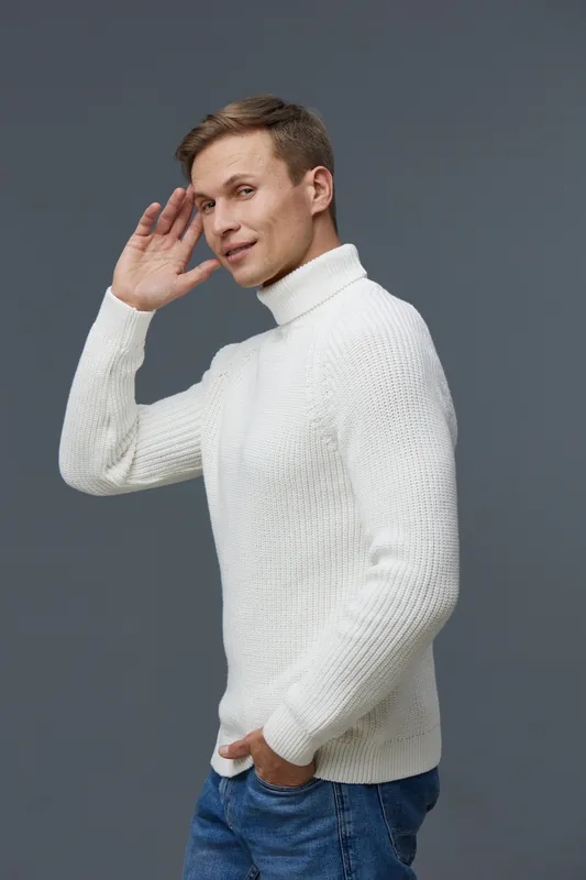 Handsome young man with short brown hair wearing white turtleneck sweater and blue jeans posing isolated on gray background studio shot. Casual fashion lifestyle concept