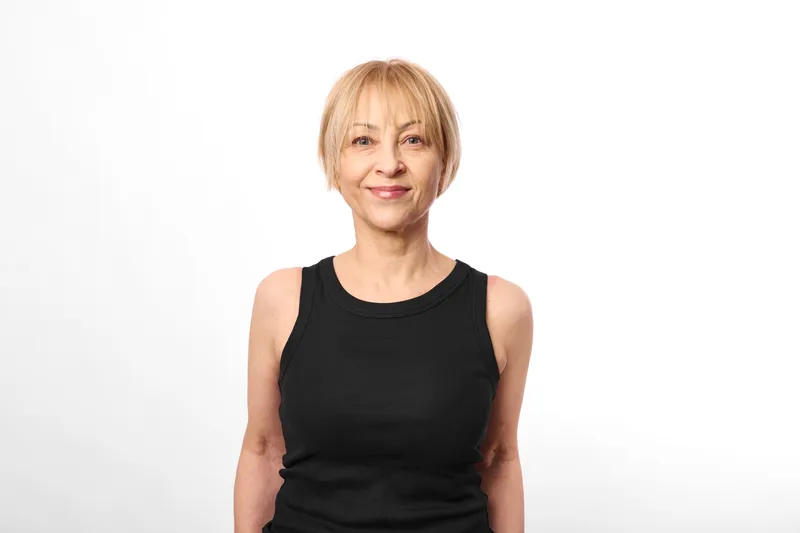 Senior woman portrait, smiling in black dress, studio photo on white background, head and shoulders view, calm friendly mood, soft light, minimal composition, natural tones