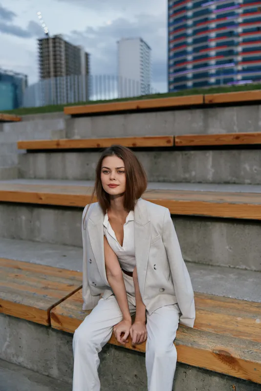 Modern woman in white suit sitting on urban stairs with confident expression during daytime business concept