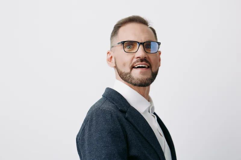 A professional man in a blazer exudes confidence and approachability on an isolated blue background, highlighting a strong business theme with emotions of focus and determination.