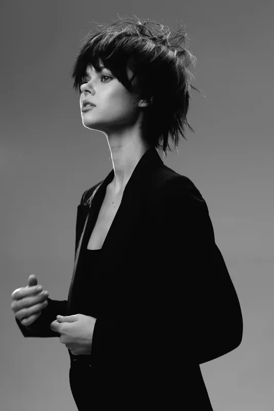Black and white portrait of a stylish woman with short hair wearing a blazer looking thoughtful indoors