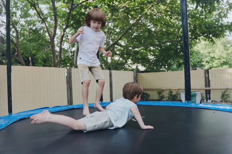 Two boys playing joyfully on a trampoline, showcasing fun and energy in a vibrant outdoor setting. The lush greenery adds to the lively atmosphere of summer.