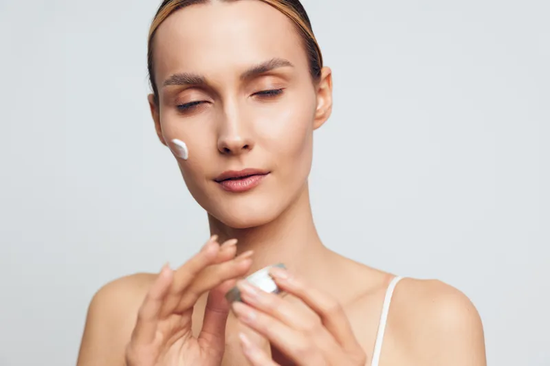 Woman skincare close up, beauty face care, cotton pad on cheeks, applying moisturizer, spa treatment, calm young woman, isolated on light background.