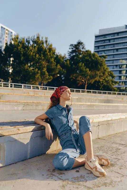 Lifestyle woman in modern boho-western denim street style sitting outdoors, relaxed with natural light and film color tones creating a warm urban vibe.
