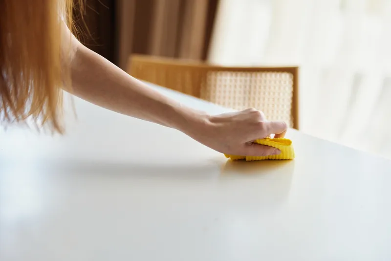 Cleaning woman wipes table with yellow sponge, hand pressing surface in bright home interior. Household chore and routine maintenance, domestic care for tidy countertop and furniture scene.