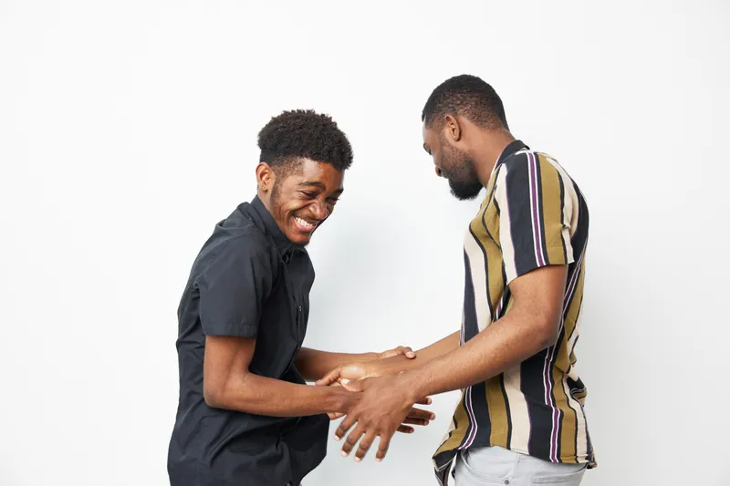 Two smiling black men sharing a joyful moment, displaying camaraderie and friendship with a modern, casual style against a clean white background.