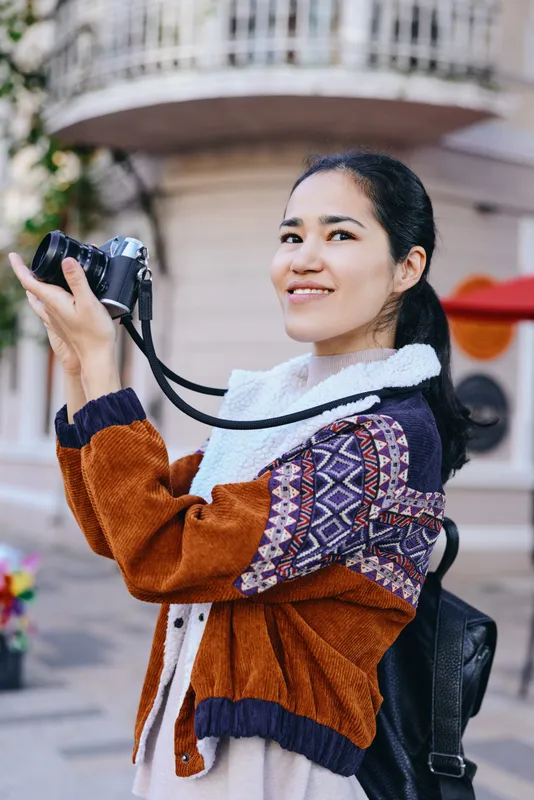 Camera, photography, outdoor, smiling, sweater, backpack, lens, urban, street, woman capturing candid moment during an outdoor city stroll with a handheld camera and curious eye for detail, ready for