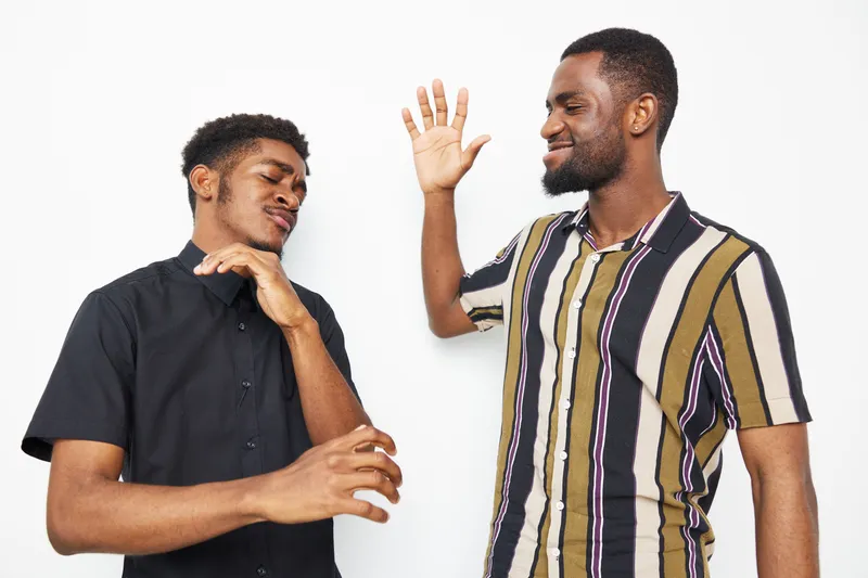 Two happy African American men enjoy a fun moment together, sharing laughter and joy in a bright, minimalistic setting. Their casual style adds to the laid-back vibe.