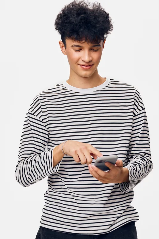 young man wearing striped shirt smiling and using smartphone, isolated on white background, casual style, technology, communication, modern life