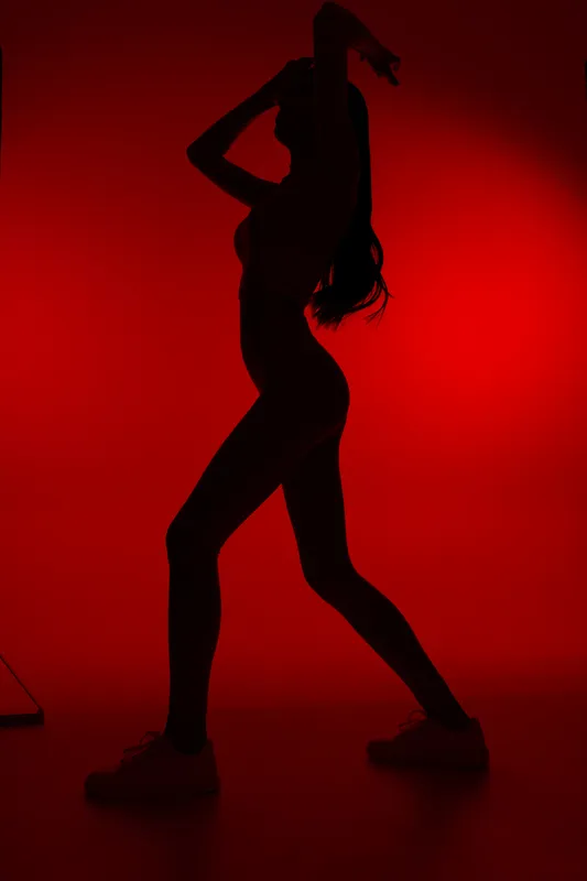 Woman sport fitness silhouette posing dynamically against a red background, showcasing strength, movement, and athletic form in a dramatic studio setting.