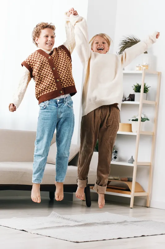 Authentic moment of children indoors, jumping with joy in cozy casual outfits, capturing spontaneous play and genuine happiness in a bright family space, everyday scene emphasizes movement, energy,