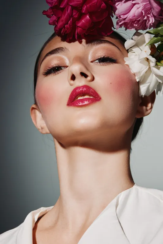 Close-up of a fashionable woman with glossy red lips and floral headpiece on a neutral background. Concept for beauty, creative makeup, and high fashion photography.