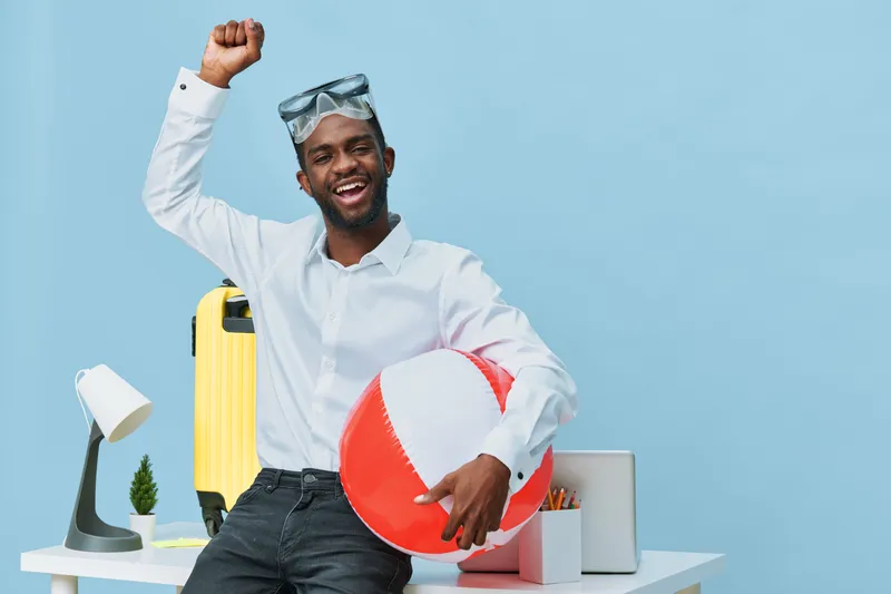 Smiling man with vacation accessories, holding a beach ball and suitcase, celebrating holiday mood in studio with travel-themed props and bright background, casual summer vacation concept.