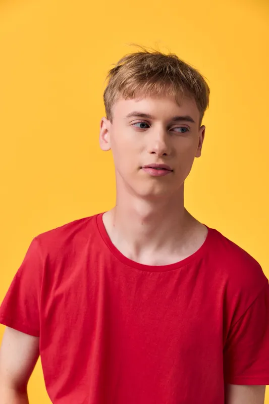 Young man in a red shirt stands before a bright yellow background, casual studio vibe, relaxed pose, clean composition and bold color contrast for modern fashion imagery