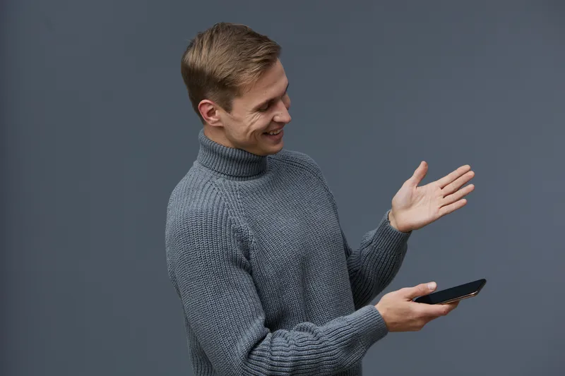smiling man using smartphone hold in hand wearing grey knitted sweater dark background digital communication concept