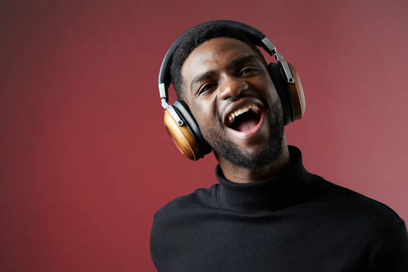 Joyful young man wearing headphones with a happy expression, against a red background, showcasing a modern lifestyle and passion for music
