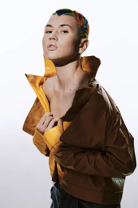 young woman with colorful hair wearing yellow jacket posing confidently against white background, showcasing edgy fashion and urban style.