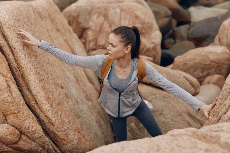 Confident young woman climbing rocky terrain in activewear, showcasing strength and determination amidst natural beauty