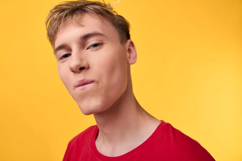 Close up of a man in a red shirt against a vibrant yellow backdrop, neutral expression, studio lighting, bold color contrast, modern style with clean, minimal composition