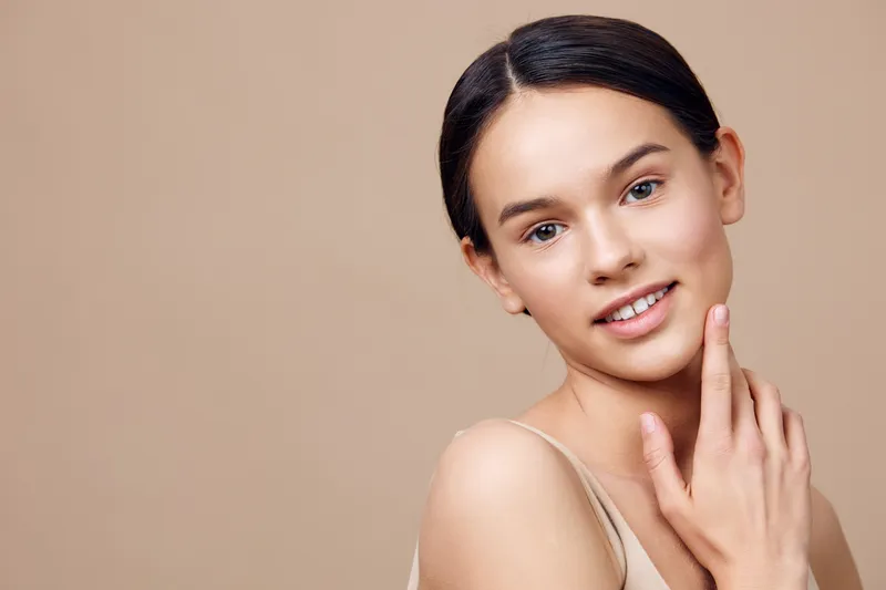 Portrait of a young woman with natural makeup and clear skin against a beige background, conveying beauty, confidence, and serenity in a minimalist style